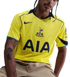Person wearing a bright yellow soccer jersey with a crest on the chest and the large 'AIA' sponsor logo across the front.
