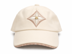 Beige baseball cap with a diamond-shaped pink embroidery on the front, centered by a small gold button on the crown.