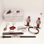 AC Milan memorabilia laid out on a white surface: tin box with Zlatan Ibrahimović image, two Milan crest cards, keychains, a red-and-black mini jersey, bracelet, necklace, pen and watch bands.