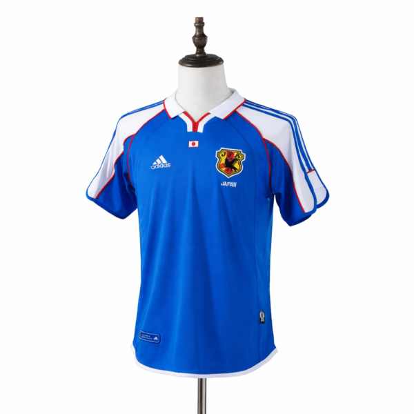 Blue Japan national soccer jersey on a dress form, featuring white shoulders, red trim, and the Japan crest with Adidas logo nearby