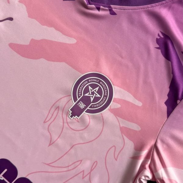 Pink and purple sports jersey with camo pattern and a circular embroidered badge featuring a star and ribbon motif on the chest area.