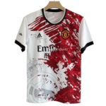 Manchester United football jersey on a hanger, white with a bold red abstract pattern, club crest on the chest and 'Fly Emirates' sponsor text.