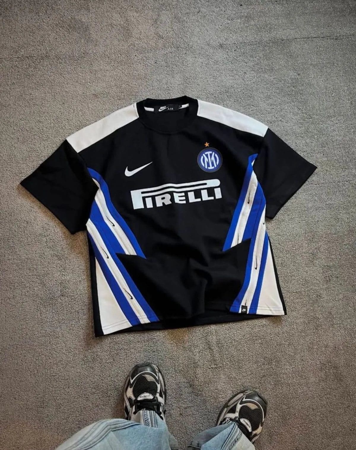 Inter Milan football jersey laid flat on a beige carpet; black with white and blue panels, featuring the Pirelli sponsor and Inter crest with a small gold star.