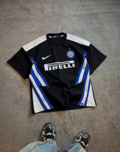 Inter Milan football jersey laid flat on a beige carpet; black with white and blue panels, featuring the Pirelli sponsor and Inter crest with a small gold star.