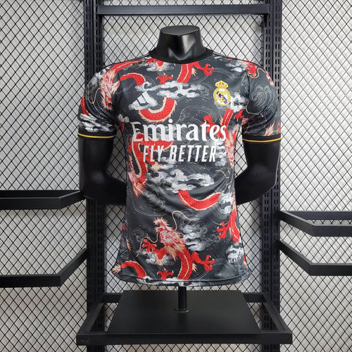 Real Madrid football jersey on a mannequin with a dragon pattern and Emirates Fly Better sponsor logo, displayed against a mesh backdrop.