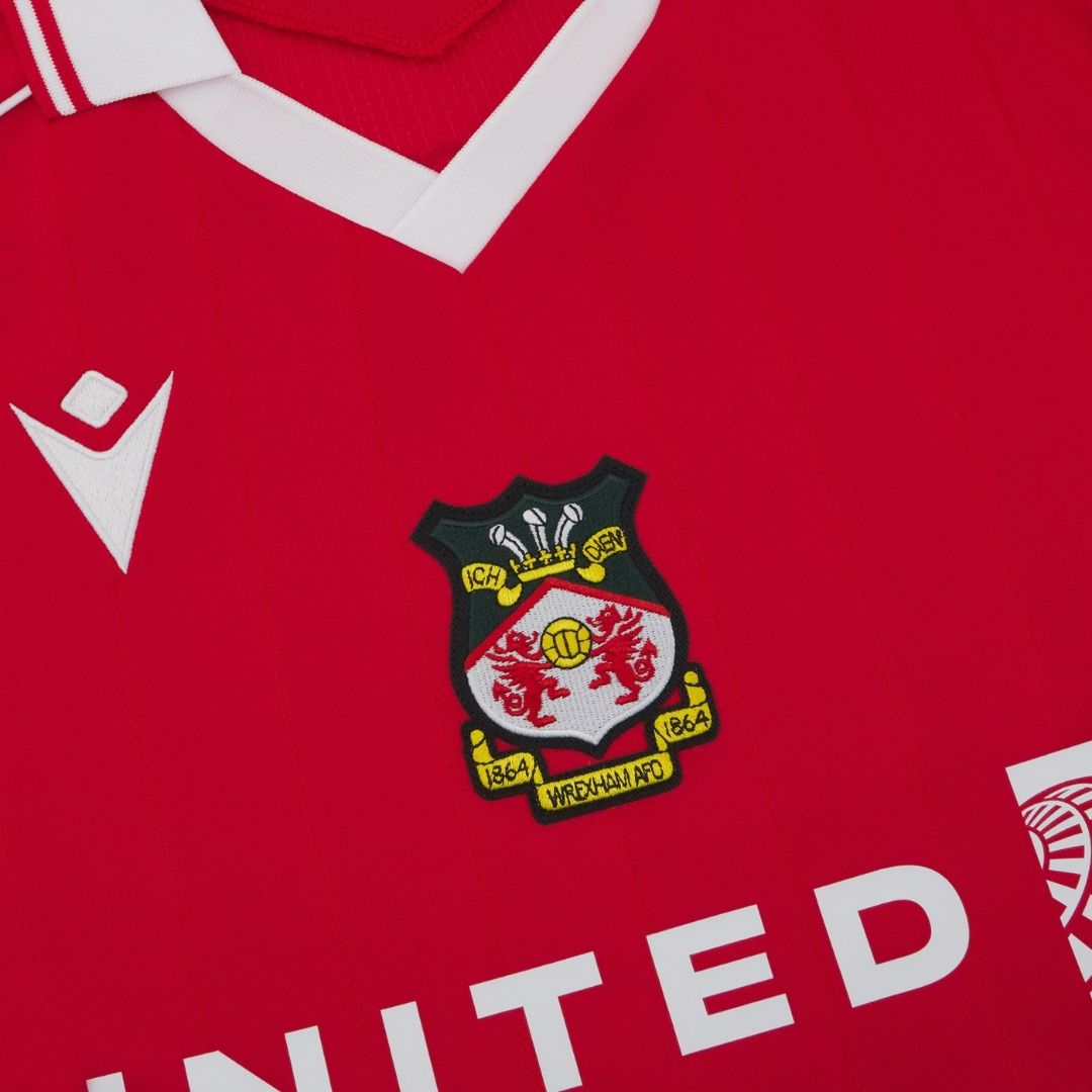 J8 | UAE SPORT STORE Close-up of a red football jersey featuring the Wrexham AFC crest and white collar trim.