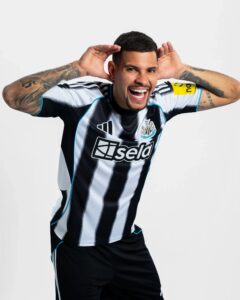 Man celebrating in a black-and-white striped soccer jersey with arms raised and hands near his head, smiling widely