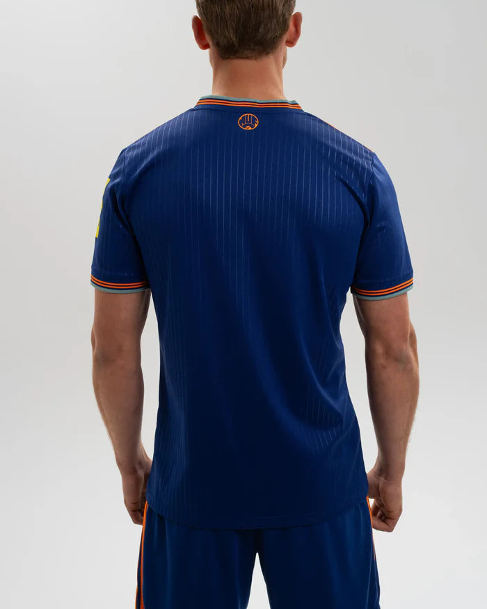 JI7388_MOD_A_ECOM_12 | UAE SPORT STORE Back view of a man wearing a blue athletic jersey with orange trim and subtle pinstripes, standing with arms at his sides.
