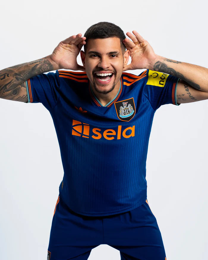 JI7388_PLAY_BG_6_1 | UAE SPORT STORE Soccer player in blue kit smiles with hands cupped behind ears, posing for the camera