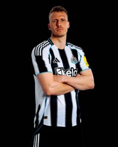 Portrait of a man wearing a Newcastle United striped jersey with arms crossed against a black background.