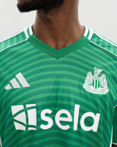 JJ2245_MOD_12 | UAE SPORT STORE Close-up of a green Newcastle United jersey with the club crest, Adidas logo, and a white sponsor wordmark across the front.