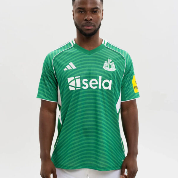 Man wearing a green striped soccer jersey with white sponsor logo 'sela' and team crest, yellow armband on the left sleeve, standing against a plain background.