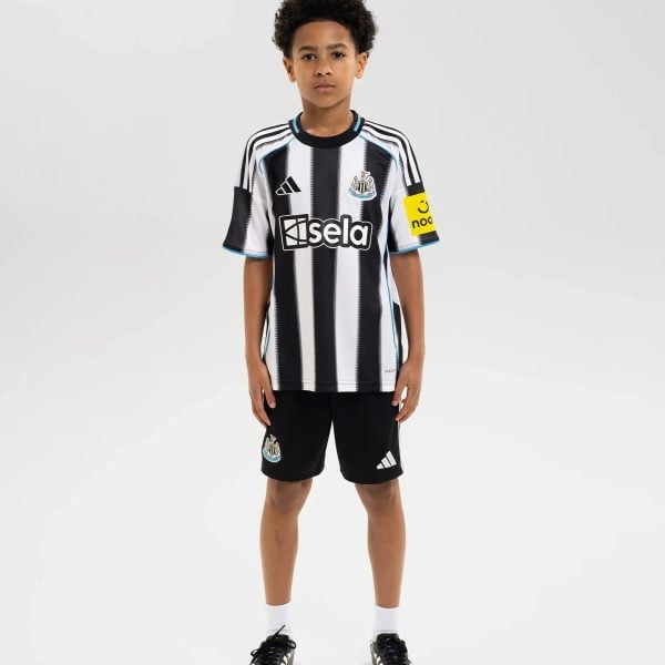 Young boy standing in a Newcastle United youth football jersey with black-and-white stripes, sponsor logo 'Isela' on chest and club crest on left side.