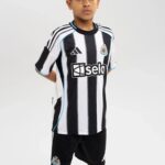 Young boy wearing a Newcastle United white-and-black striped football jersey with the club crest on the chest and Adidas logo on the other side.