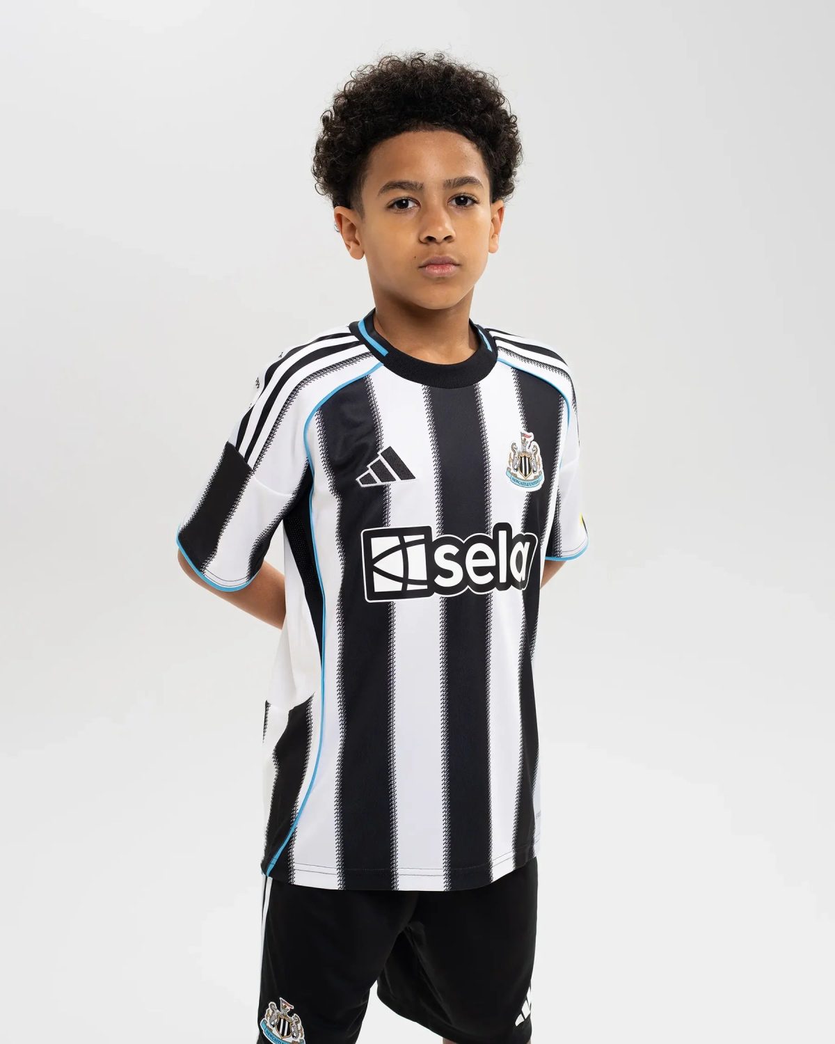 Young boy standing and looking at the camera, wearing a Newcastle United black-and-white striped soccer jersey.
