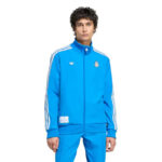Blue Real Madrid track jacket with white stripes and matching pants worn by a model; features Adidas logo and Real Madrid crest on the chest.