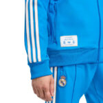 Close-up of a royal blue Real Madrid tracksuit with white Adidas stripes on the sleeve and team crest on the pants.