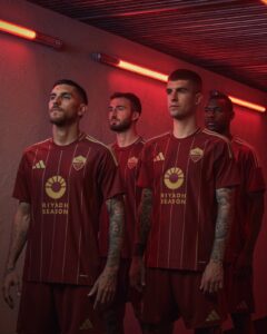 Four male soccer players in maroon uniforms stand in a red-lit hallway, posing for a team photo.