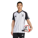 Male model wearing a white Juventus football jersey with black pinstripes, holding a soccer ball at his side.