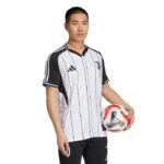 Male model wearing a white and black striped Juventus soccer jersey, holding a red–white soccer ball at his side.