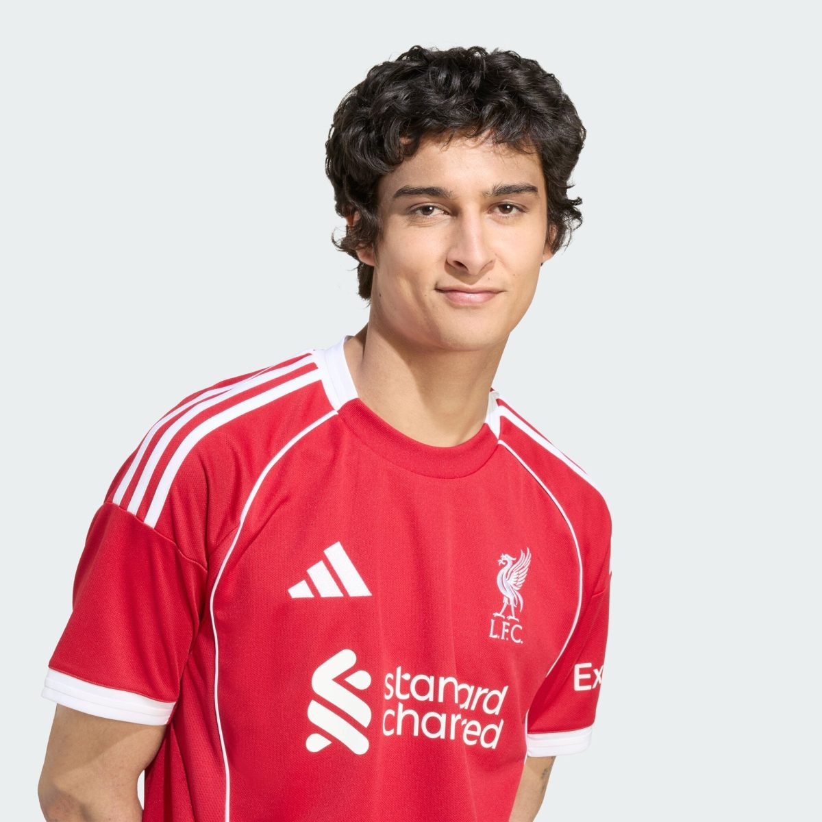 Young man wearing a red Liverpool FC jersey with white Adidas stripes, facing the camera.