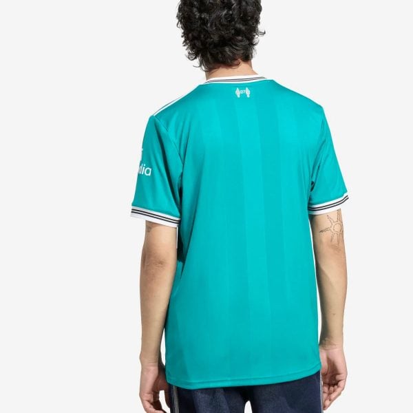 Back view of a person wearing a teal jersey with white striped trim, crest near the neck, and subtle vertical panels; visible tattoo on the right forearm.