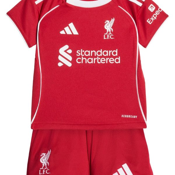 Red Liverpool FC football jersey with white Adidas stripes on the shoulders, crest, and sponsor logos (Standard Chartered) visible; paired with matching red shorts showing club emblem.