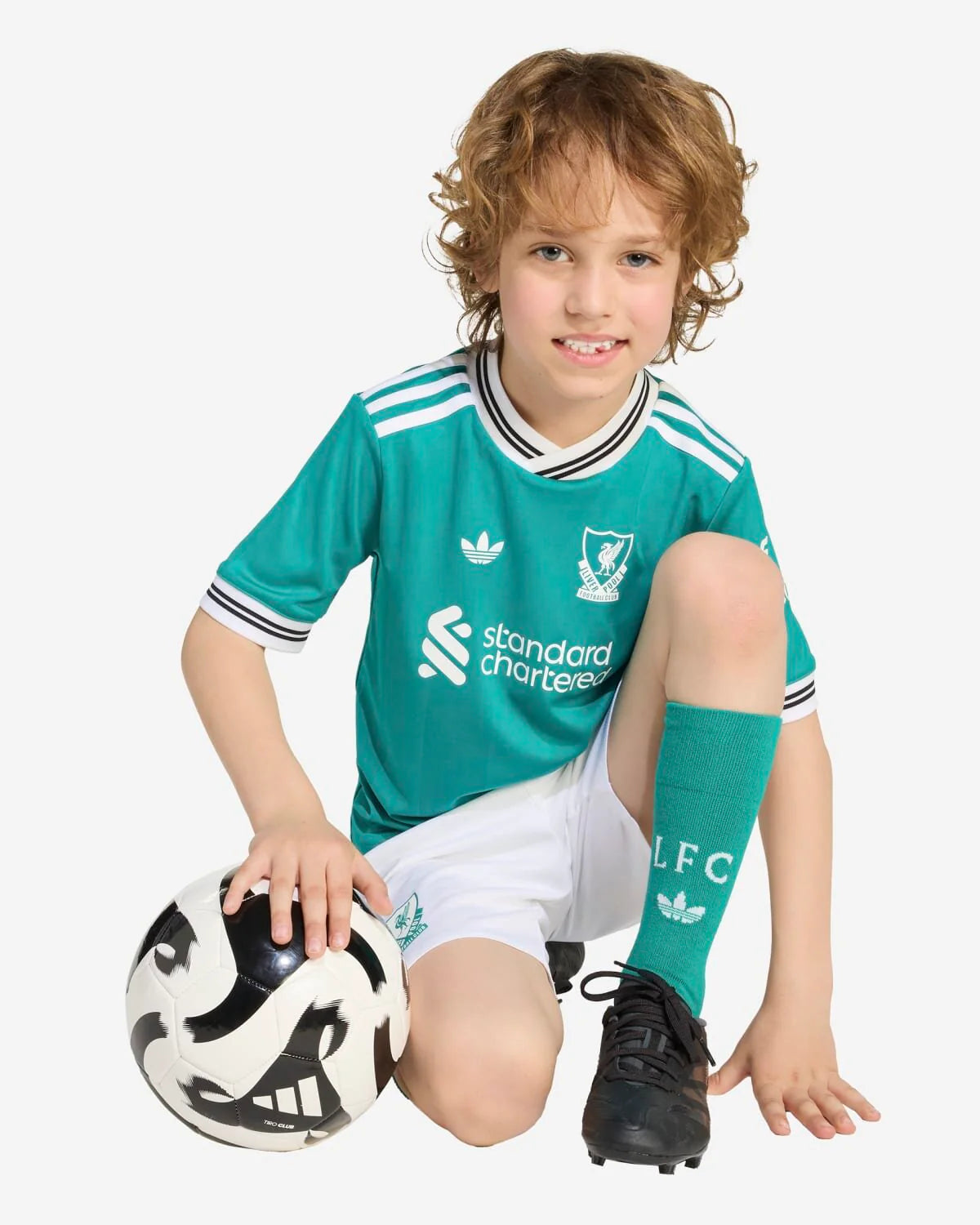 JV6470_4_APPAREL_OnModel_WalkingView_custom_1-lowres | UAE SPORT STORE Young boy in teal Liverpool FC jersey kneeling with a soccer ball at his side on a white background.