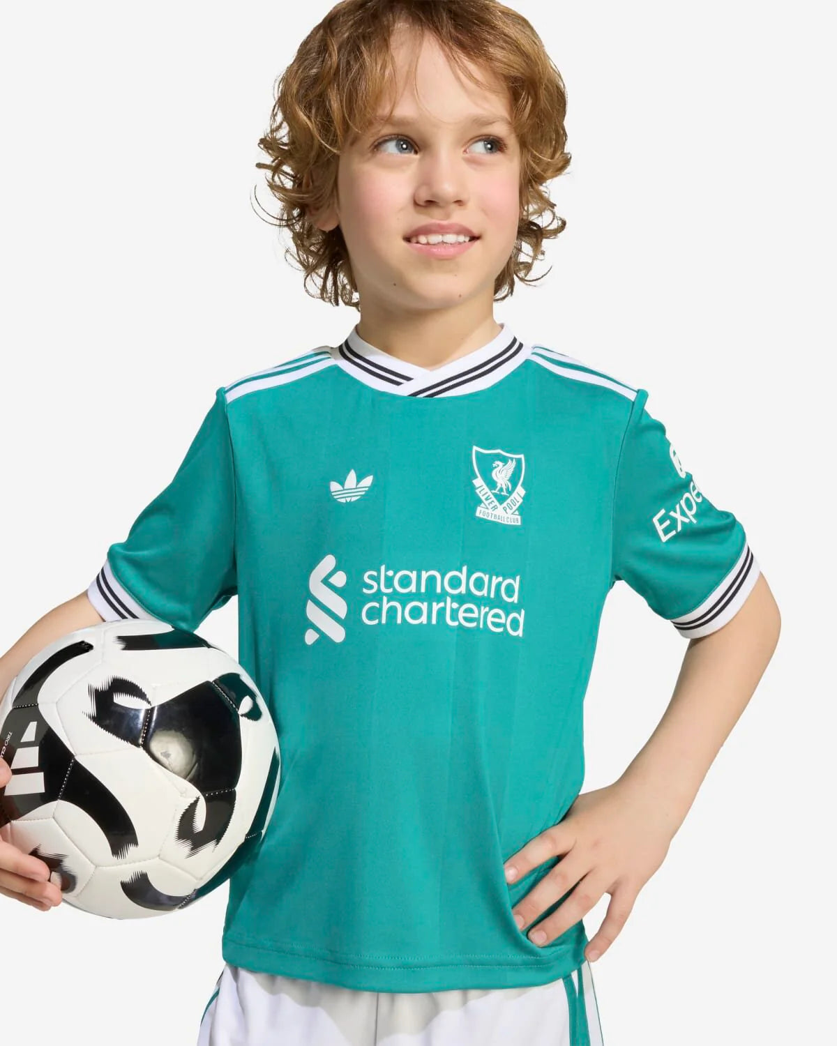 JV6470_5_APPAREL_OnModel_DetailView1_custom_1-lowres | UAE SPORT STORE Young boy in a teal Liverpool FC jersey holding a soccer ball at his side, looking off to the right mainly.