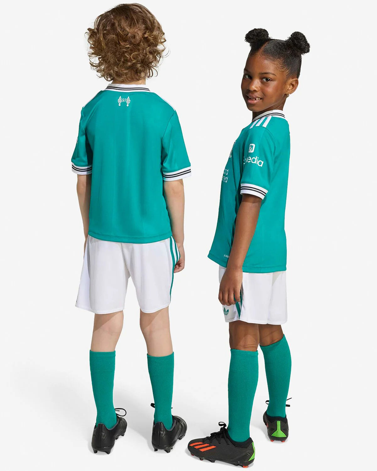 JV6470_7_APPAREL_OnModel_StandardUnisexBackView_grey_1-lowres | UAE SPORT STORE Two children in teal soccer uniforms stand back-to-back on a white backdrop, wearing teal jerseys, white shorts, teal socks, and black cleats.