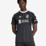 JV6477_4_APPAREL_OnModel_StandardView_custom_1-lowres | UAE SPORT STORE A man wearing a black Liverpool FC jersey with white stripes, sponsor logo, and crest, posing against a light background.