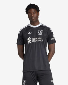 A man wearing a black Liverpool FC jersey with white stripes, sponsor logo, and crest, posing against a light background.