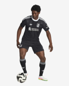 Liverpool FC player in a black away kit dribbling a soccer ball at his feet.