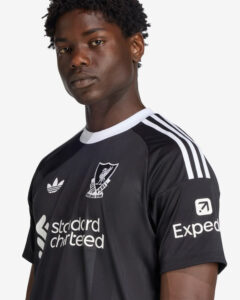 Portrait of a man wearing a black Liverpool FC training jersey with white stripes on the shoulders and sponsor logos.