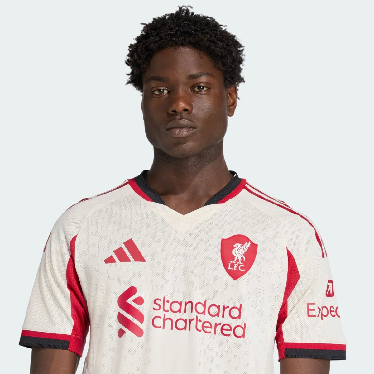 Close-up of a person wearing a white Liverpool FC football jersey with red accents and sponsor logo.
