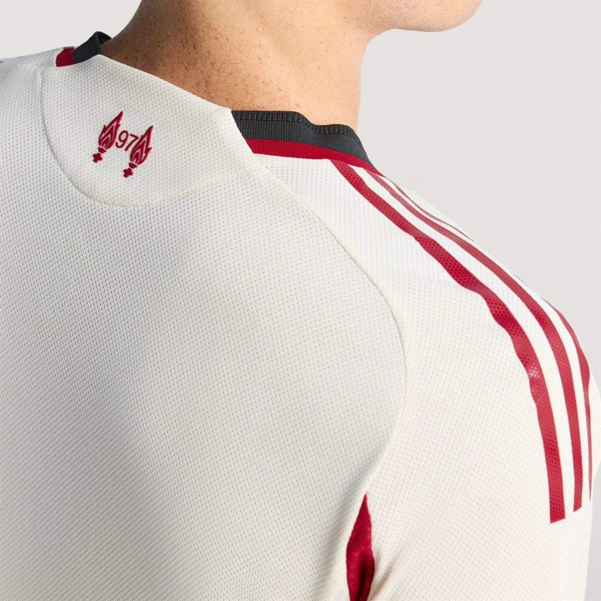 Close-up of a white perforated sports jersey back with red stripes along the shoulder and a small red emblem near the collarbone area.