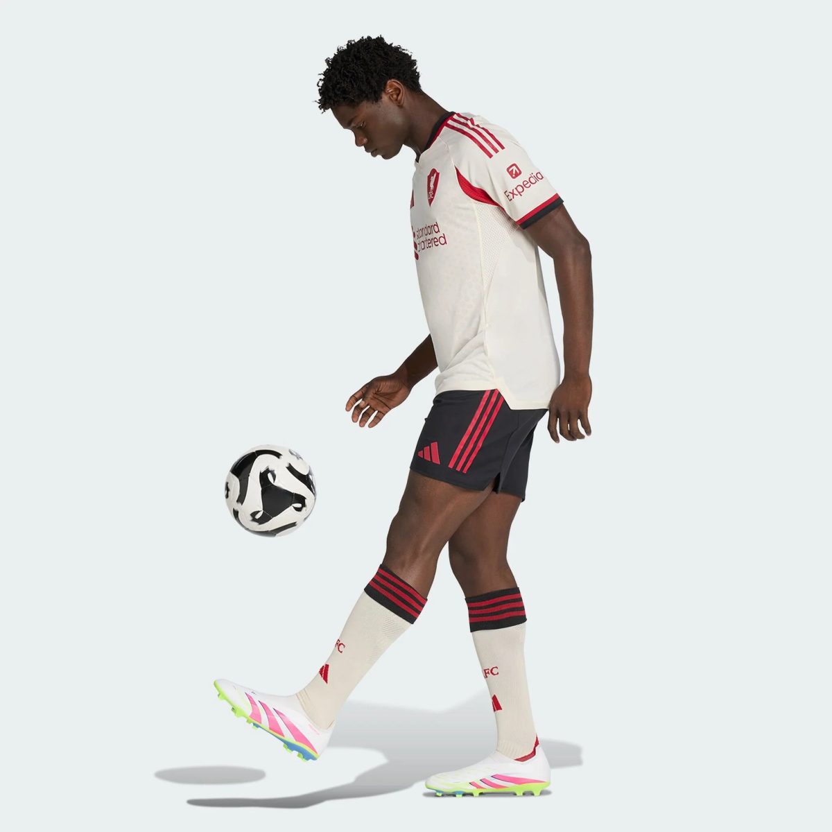 Soccer player in a white jersey and black shorts kicking a soccer ball in mid-action.