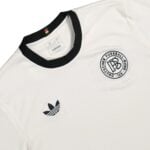 Close-up of a white Adidas jersey with a black collar, subtle pinstripes, and a circular team crest.