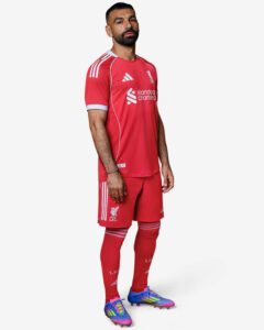 Professional soccer player in red Liverpool FC kit, standing in profile, wearing colorful cleats.