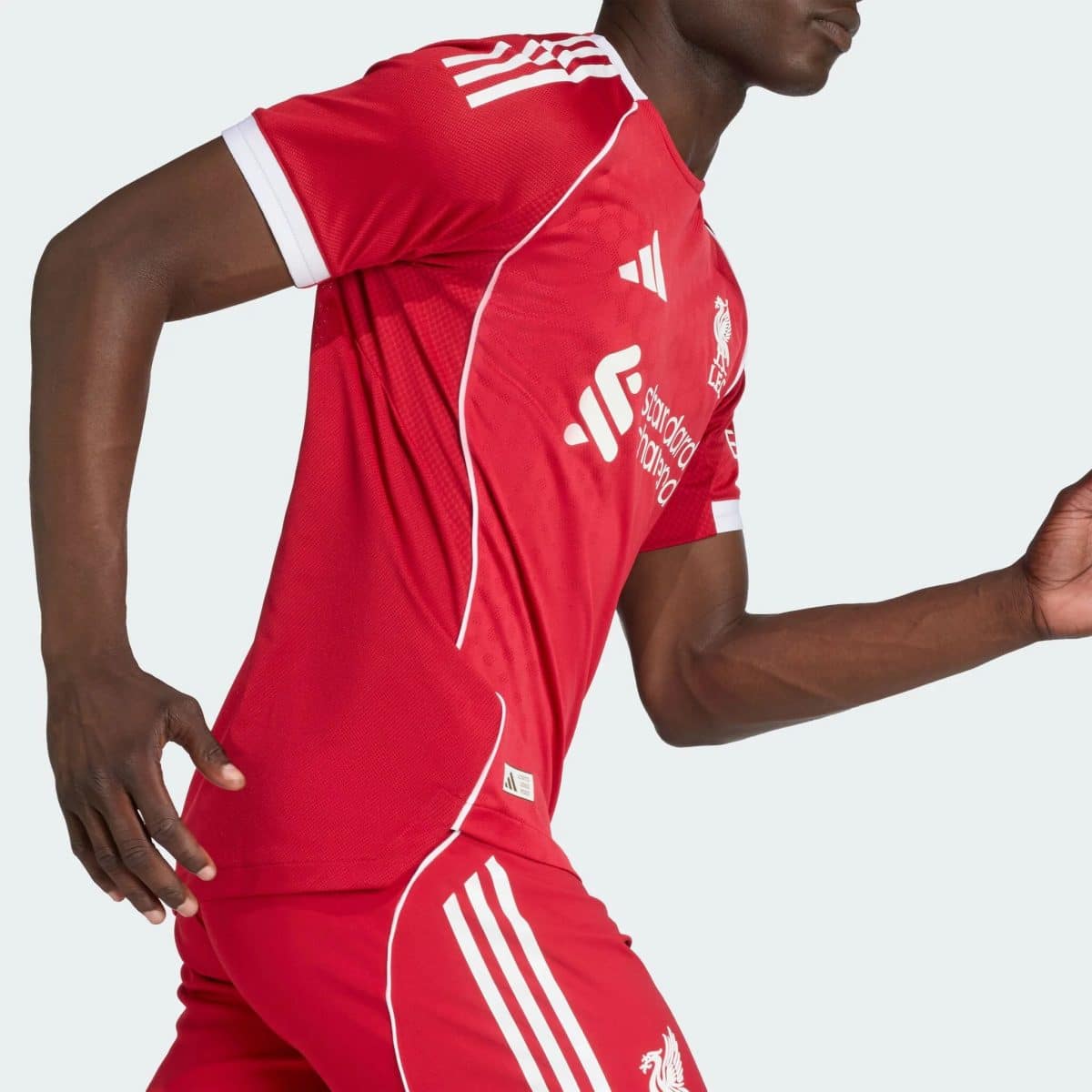 Side view of a person wearing a red athletic jersey with white stripes and crest, mid-motion against a light background.