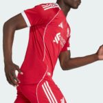 Side view of a person wearing a red athletic jersey with white stripes and crest, mid-motion against a light background.