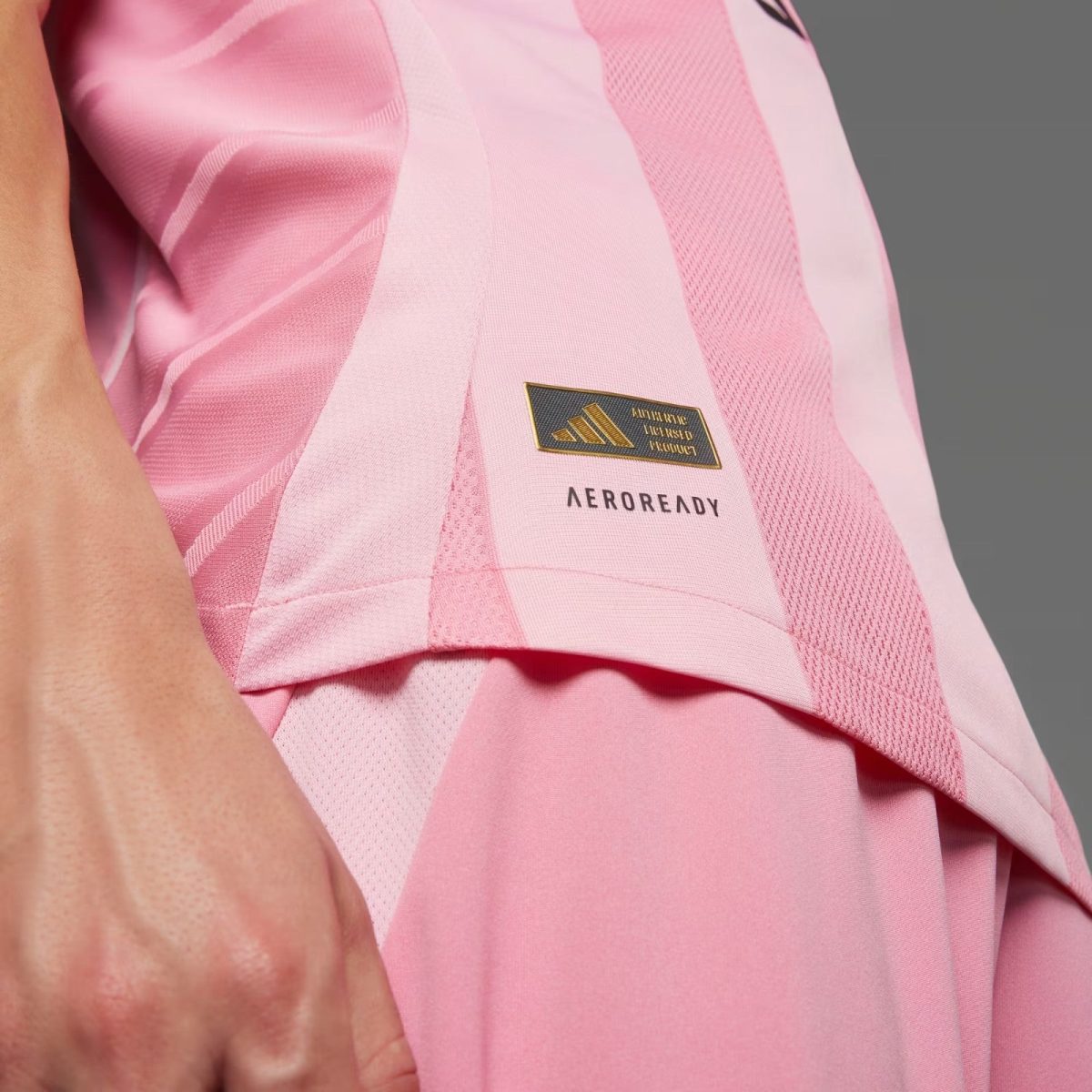 Close-up of a pink athletic shirt showing the Adidas Aeroready tag and logo on the chest area, highlighting the fabric texture.