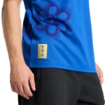Close-up of a blue athletic shirt with a purple floral motif and a small gold brand label near the hem.