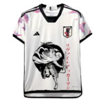 White Japan national soccer jersey with a bold black anime-style warrior illustration on the front and red vertical Japanese text on the right panel.