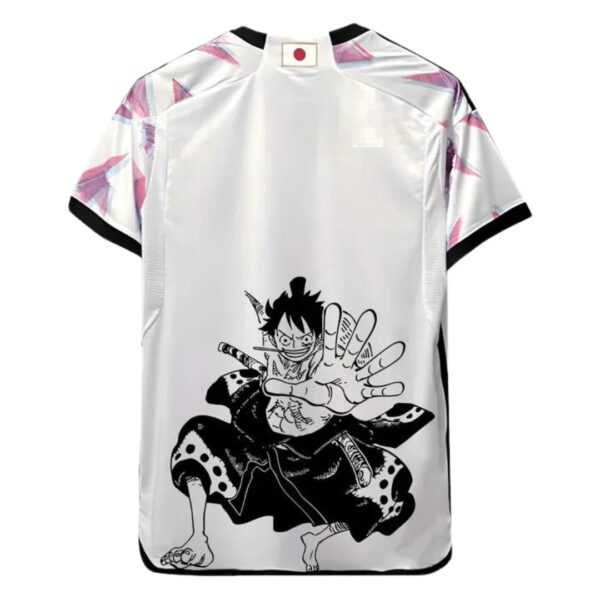 Back view of a white athletic jersey with pink angular sleeve patterns, black cuffs, and a large black Luffy illustration reaching forward on the back, near the hem, with a small Japanese flag at the collar.