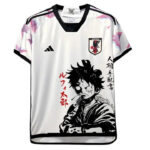 White soccer/football jersey with black trim featuring a large black-and-white manga-style portrait of a young man, red vertical Japanese text on the left, JFA crest on the chest, and an Adidas logo on the opposite side.