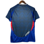 Back view of a blue sports jersey with dark central panel, blue side panels, and red accents; features a white signature 'UZUMYI' near the bottom.