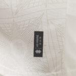 Close-up of light patterned fabric with a small black rectangular brand tag featuring a white geometric logo.