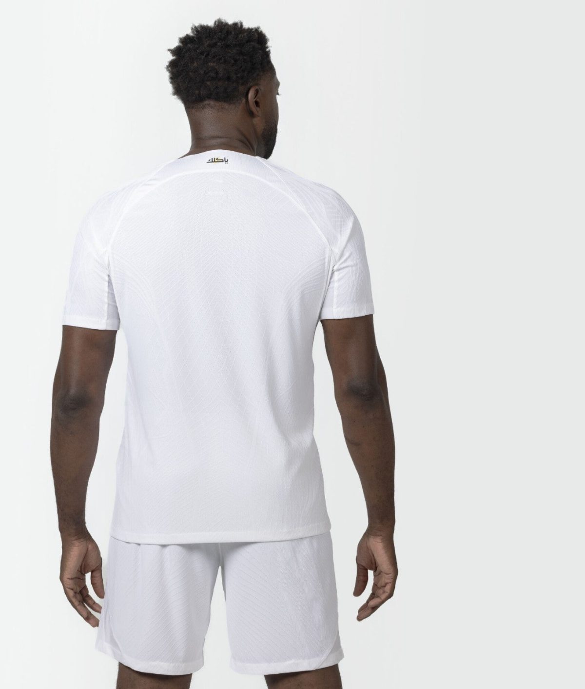 Back view of a man in a white athletic t-shirt and shorts, small logo near the neckline on the back.