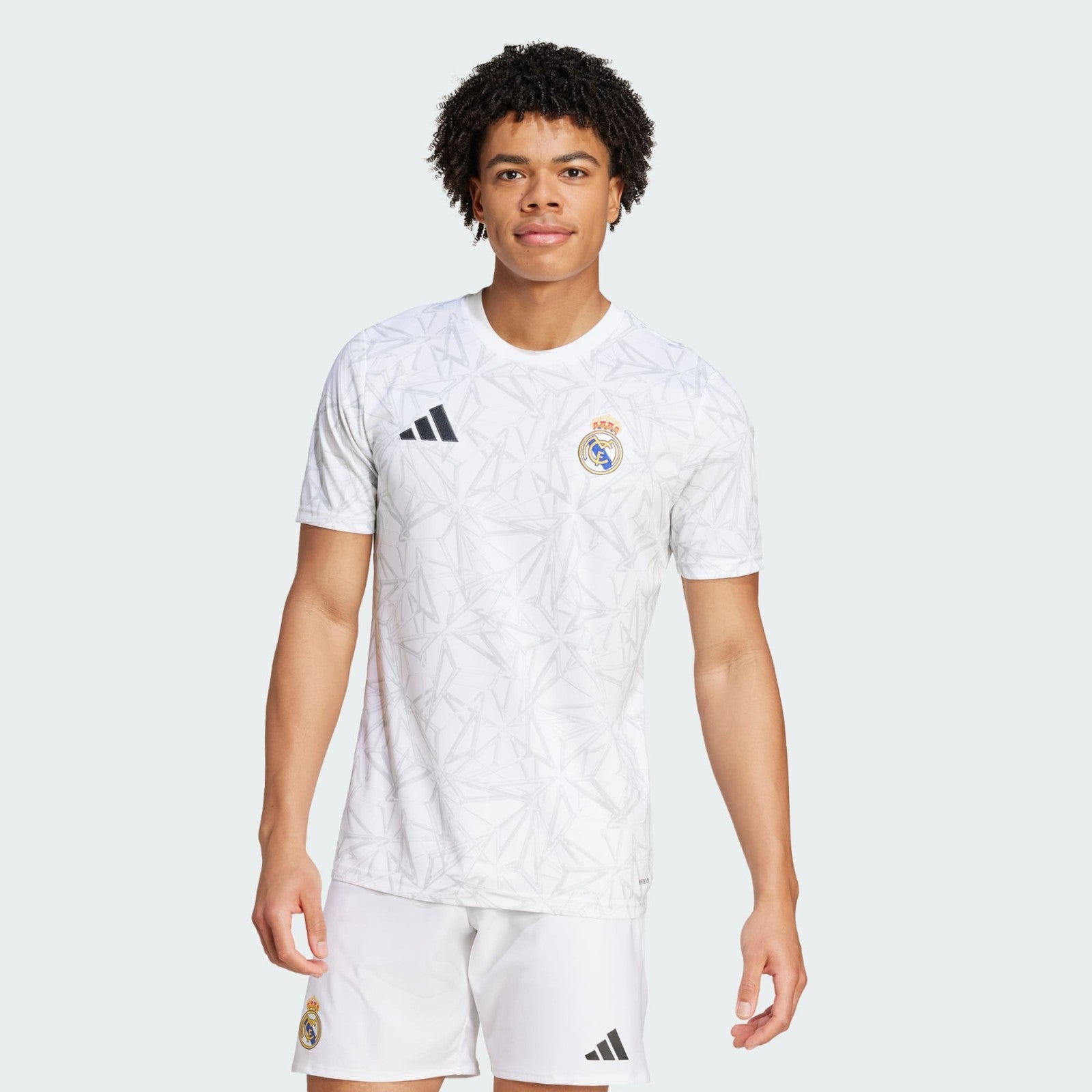 K5bULrDYmEiumKB | UAE SPORT STORE Young man modeling a white Real Madrid football jersey with Adidas logo against a pale background.